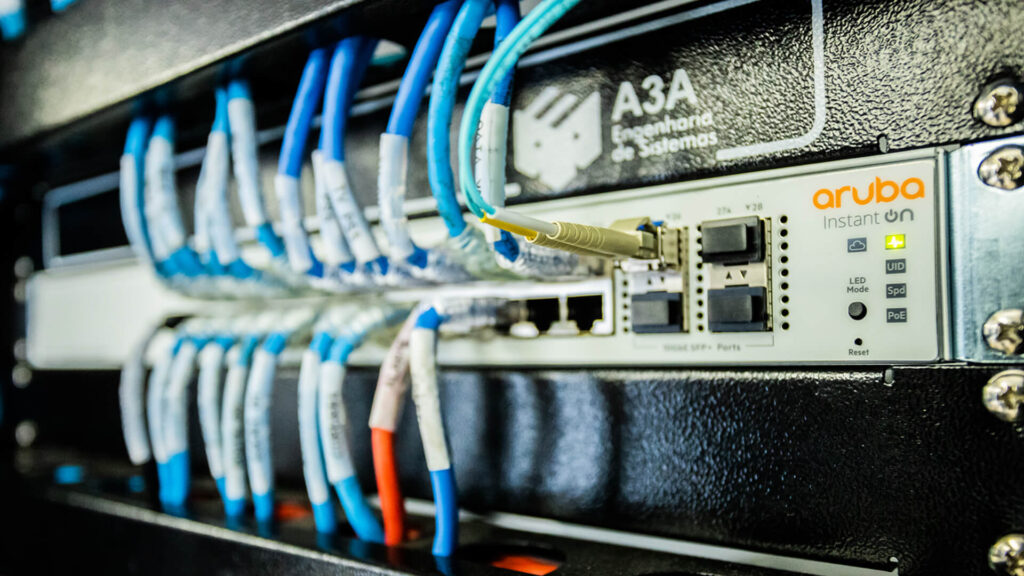 A imagem mostra um close-up de um switch de rede, com vários cabos Ethernet conectados às suas portas. O foco está na tecnologia e na conectividade, destacando a infraestrutura física que permite a comunicação em rede. Os cabos estão organizados e etiquetados, indicando uma configuração de rede bem gerenciada. Essa imagem é relevante para ilustrar equipamentos de rede em uso, essenciais para a conectividade de internet e intranet em diversos ambientes, como escritórios ou data centers.