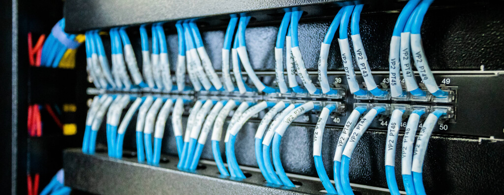 Imagem de cabos de rede organizados e etiquetados em um patch panel, representando uma instalação de cabeamento de rede de alta qualidade. A imagem destaca a organização e a eficiência no gerenciamento de cabos, elementos cruciais para um sistema de cabeamento de rede confiável e bem estruturado