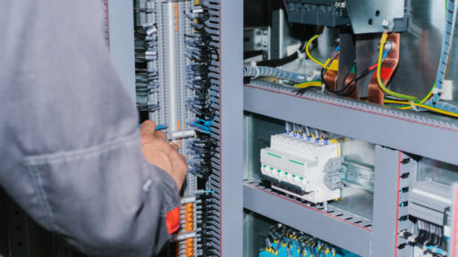 Técnico realizando manutenção em quadro elétrico com barramentos, cabos e disjuntores em instalação elétrica de baixa tensão